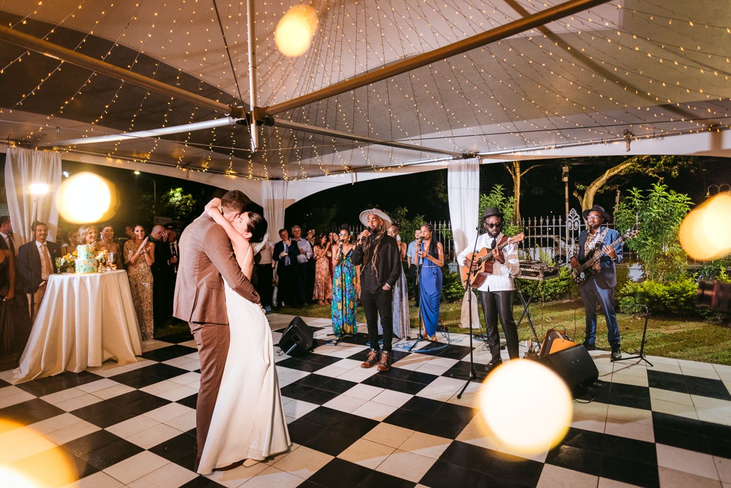 A black and white checkered dance floor illuminated by string lights at an elegant outdoor wedding reception.