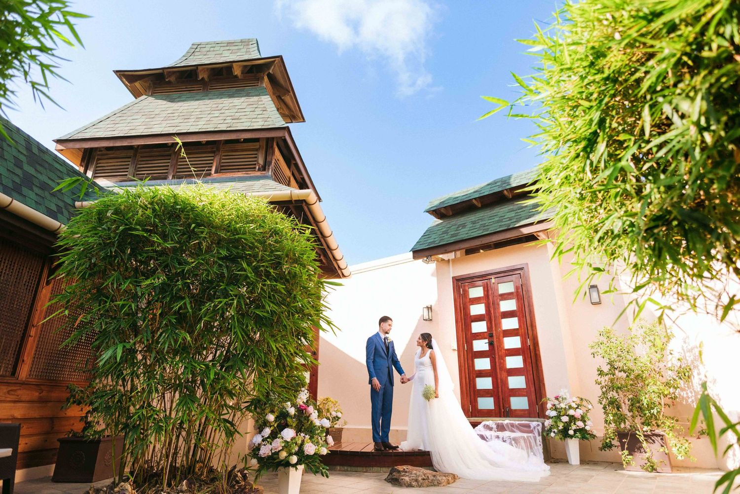 Asian temple architecture with bamboo trees and traditional red details against blue sky.
