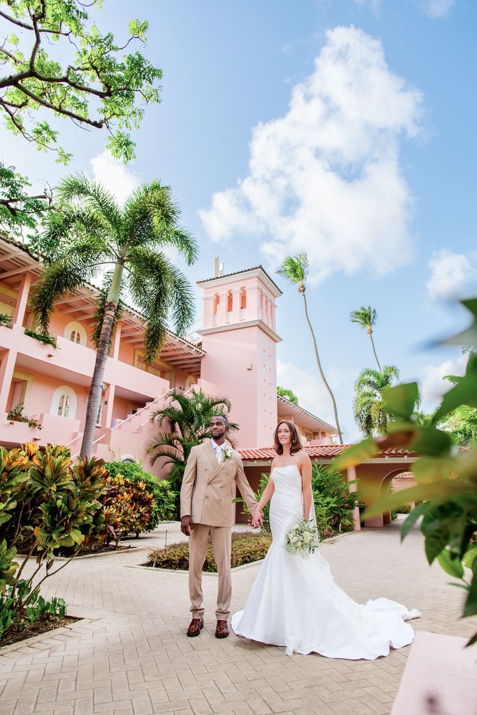 Wedding portraits taken against pink Spanish colonial architecture with palm trees.