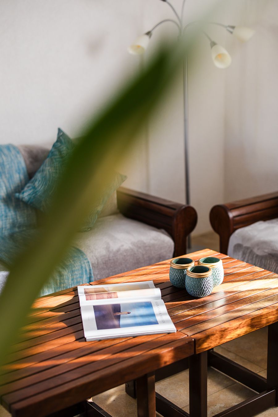 Wooden coffee table with teal ceramic cups and a magazine in a cozy living room with dark wood chairs and soft cushions.