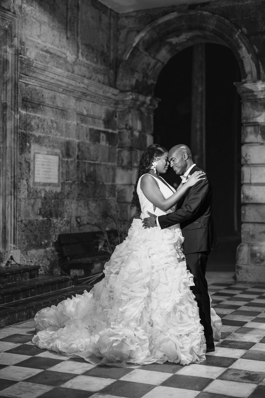 Black and white photo of a bride and groom sharing an intimate moment in a historic stone building with checkered floors.
