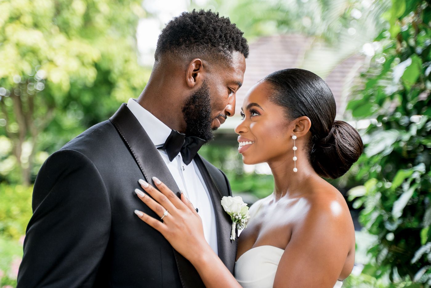 Elegant Black couple nearly kissing on their wedding day outdoors, bride in strapless gown and groom in black tuxedo.