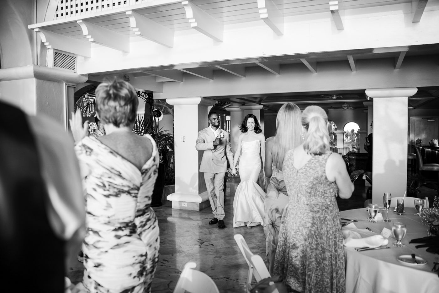 Black and white photograph of wedding guests dancing and celebrating at an indoor reception.