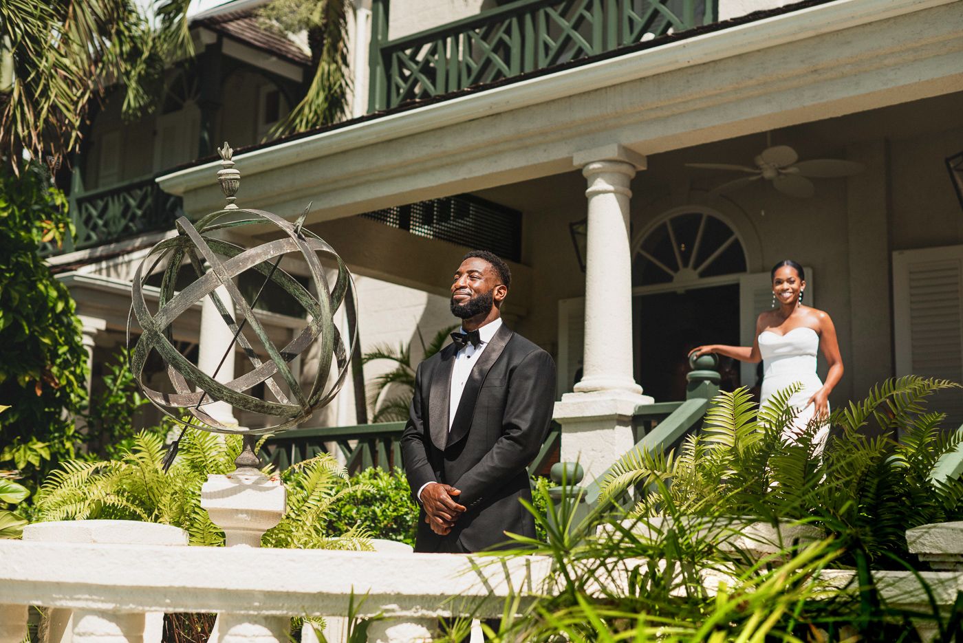 First look wedding moment on classic white columned porch surrounded by tropical foliage.