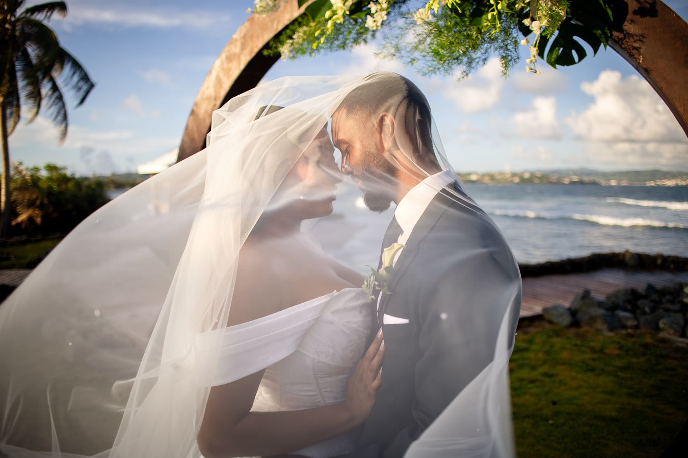 Romantic beach wedding portraits with flowing veil against tropical oceanfront backdrop.