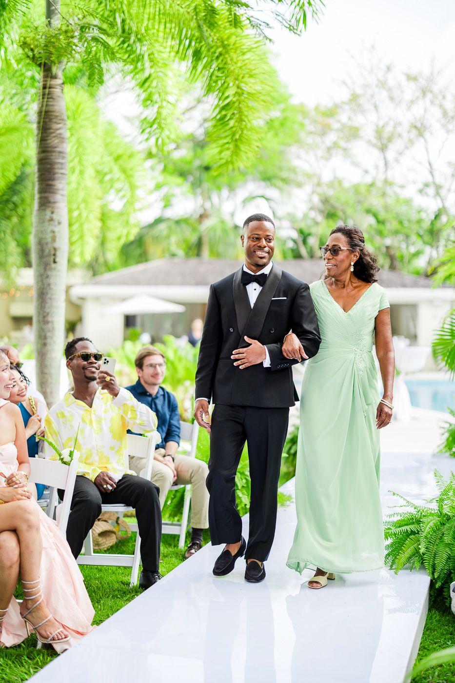 Wedding party members pose playfully outdoors with palm trees and mint green attire.