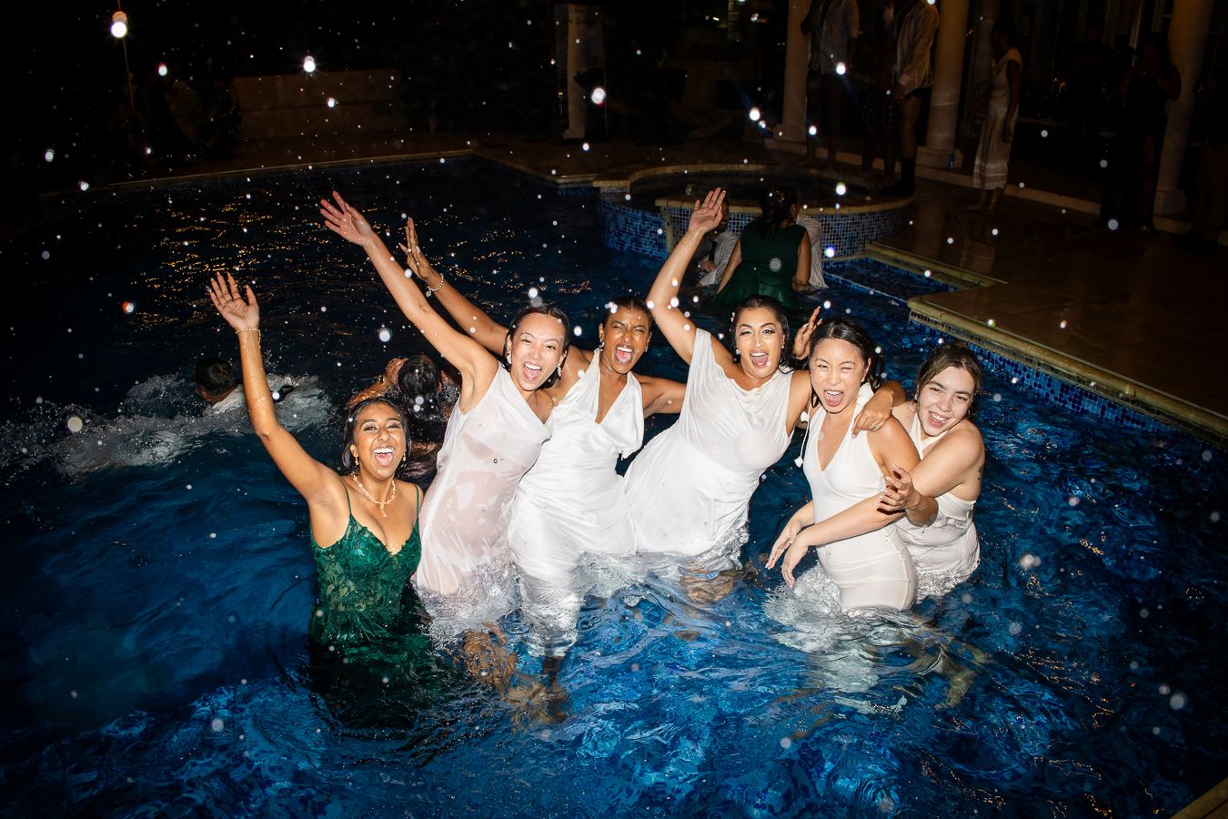 Celebratory group splash in illuminated pool during nighttime wedding festivities.