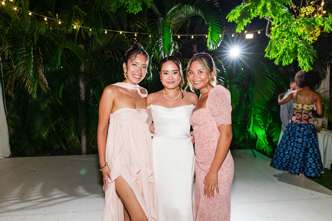 Guests enjoy dancing and mingling at an evening wedding reception with green tropical backdrop.
