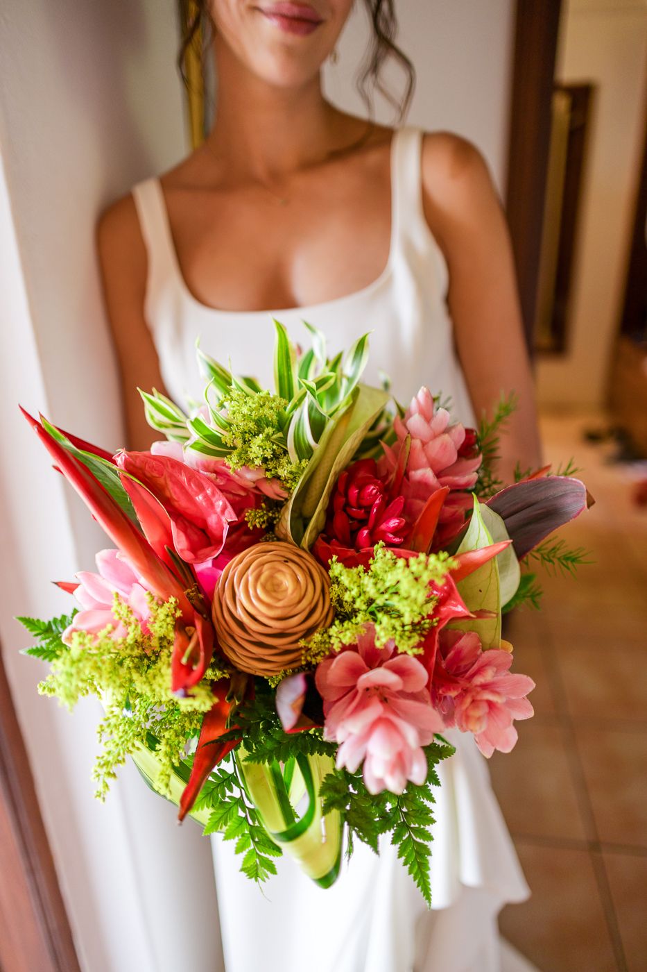 Vibrant tropical wedding bouquet featuring pink lilies, red roses, and green foliage.