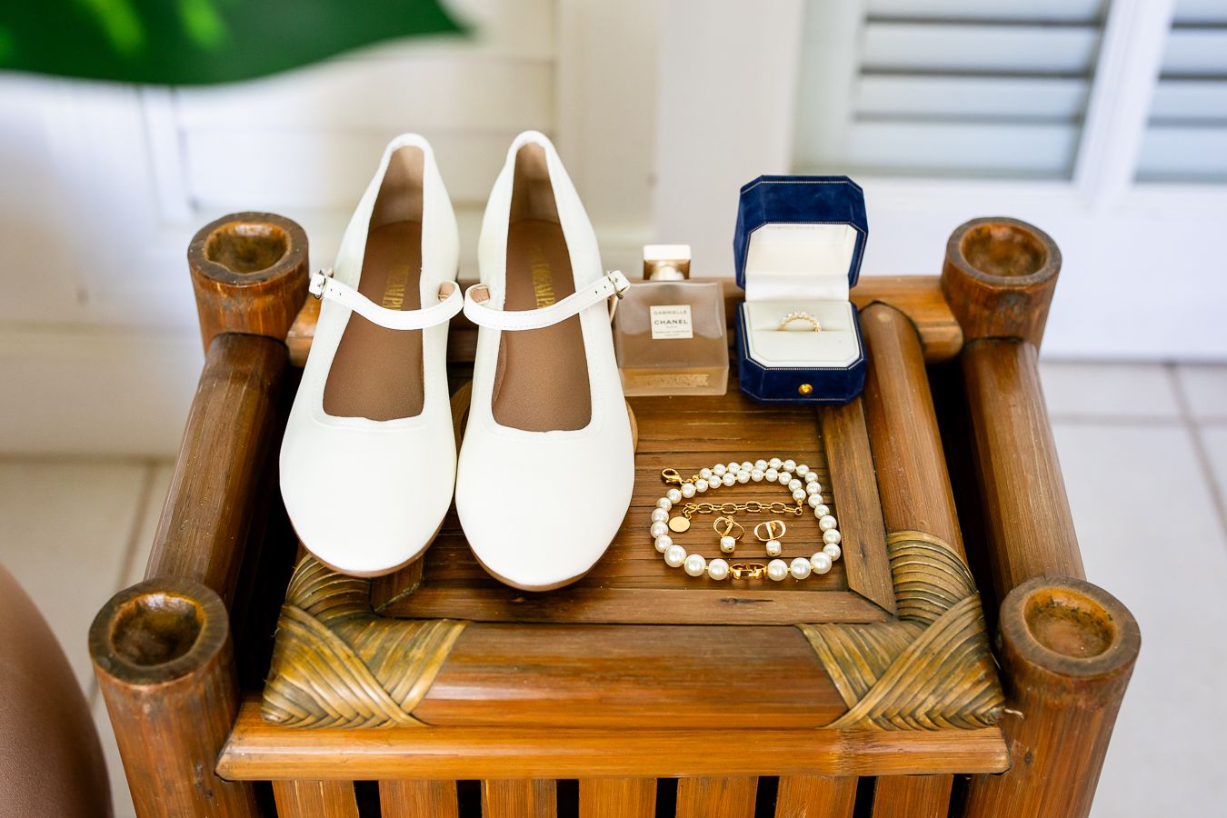 Wedding accessories including white Mary Jane shoes, pearls and ring box displayed on wooden table.