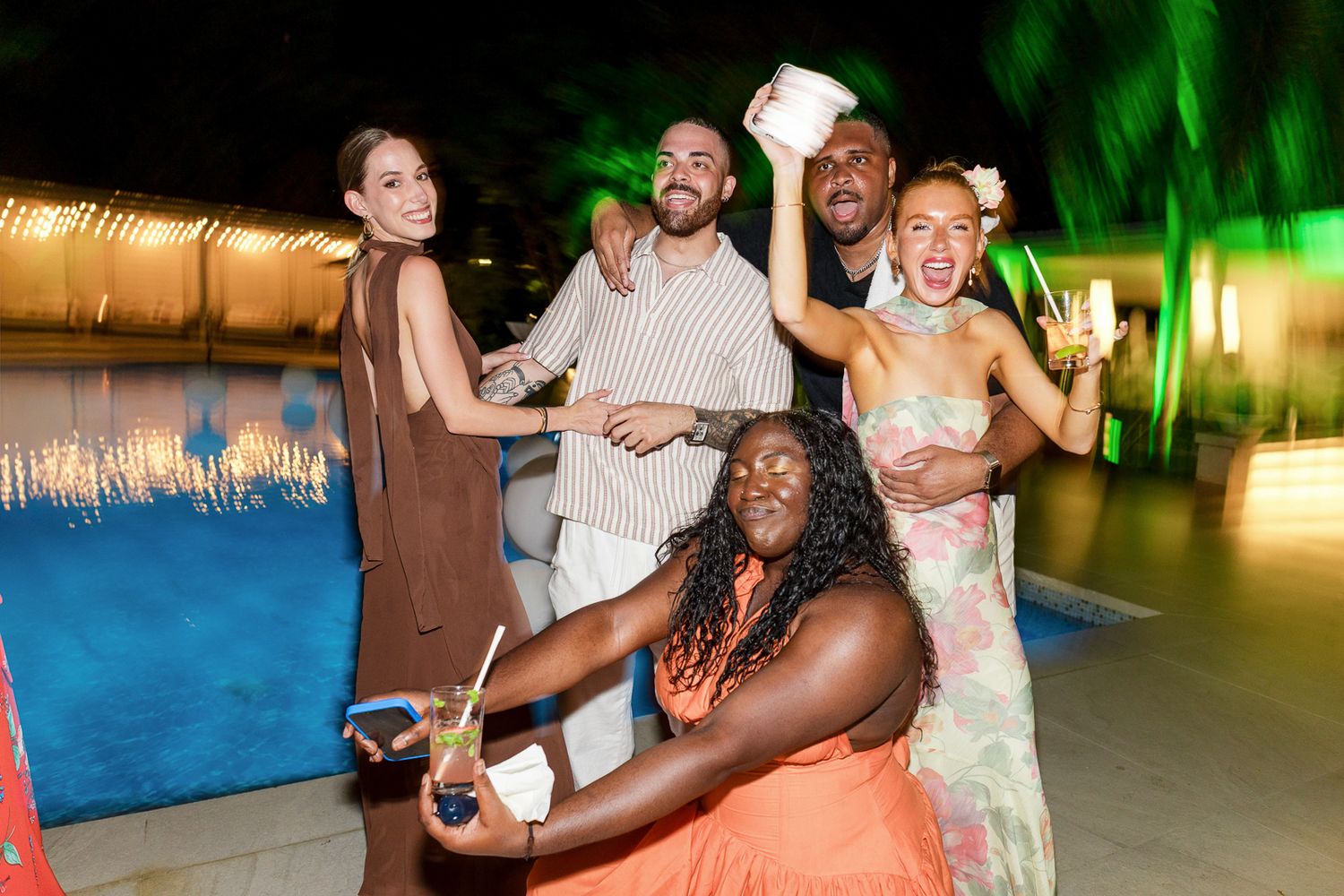 People dancing and celebrating at a festive outdoor party with green lighting and tropical decor.