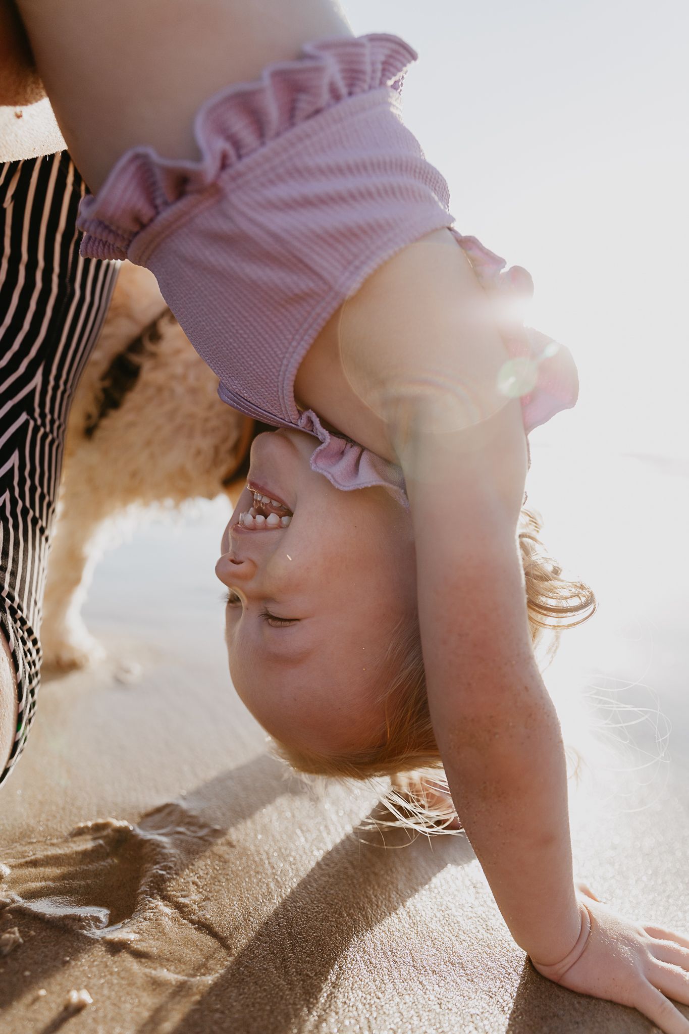 Baby in pink ruffled outfit crawls across carpet in sunlit room.