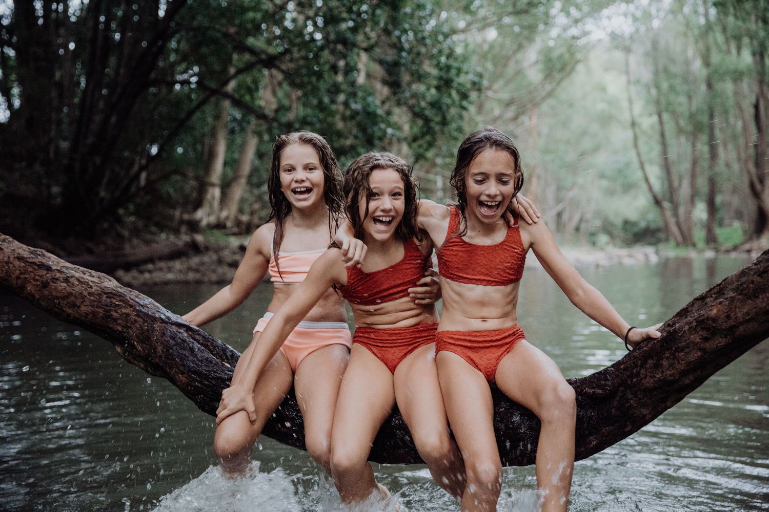 People sitting together on a tree branch over water during an outdoor photo session.