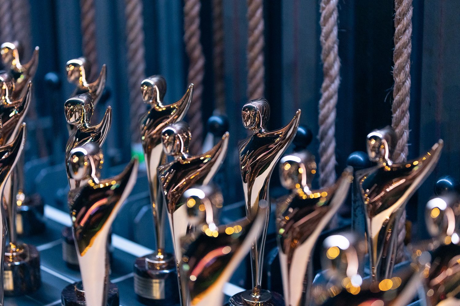 Row of golden AACTA award trophies displayed on blue background.