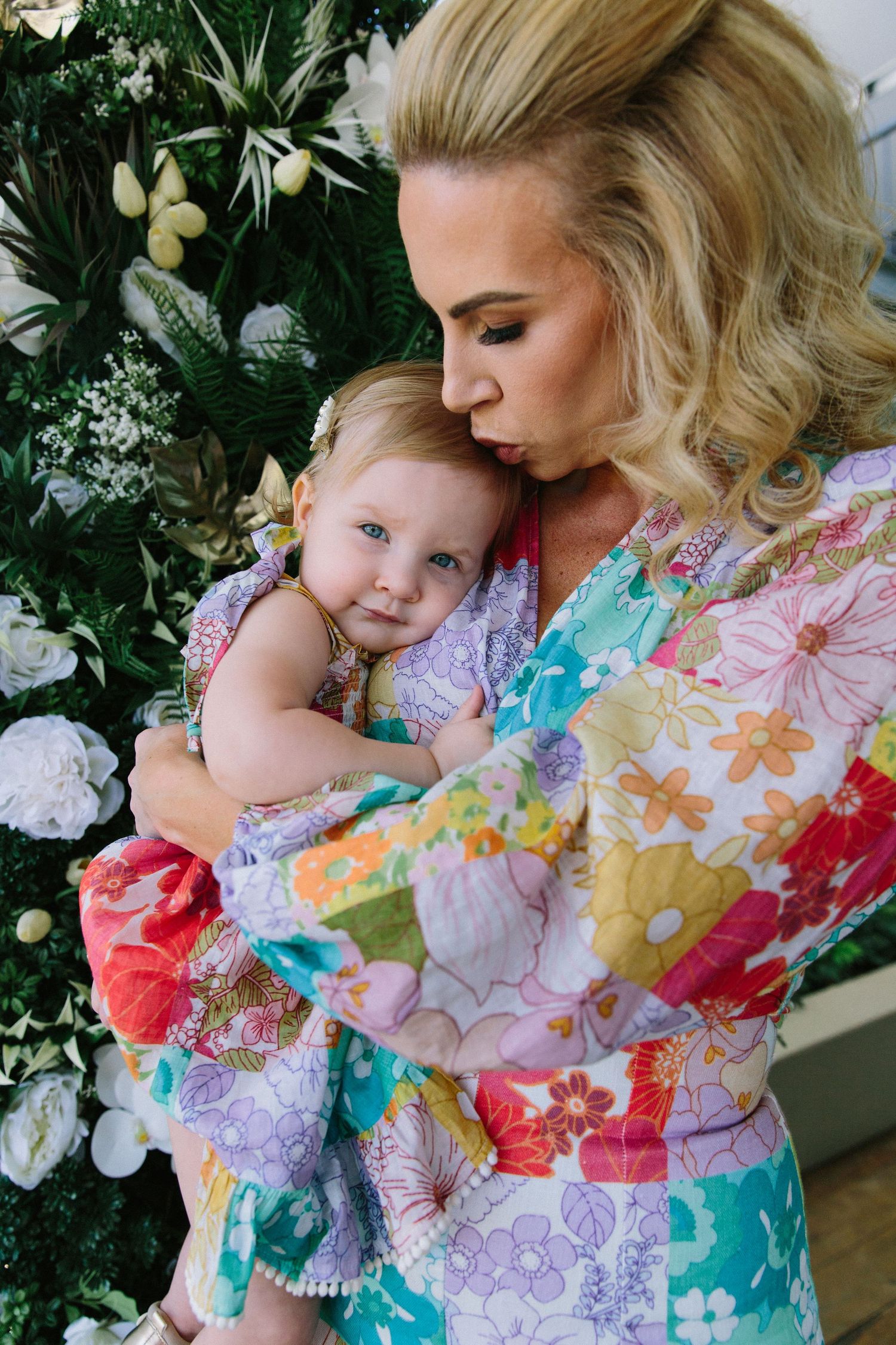 Mother and child share tender moments against floral backdrop in colorful summer dresses.