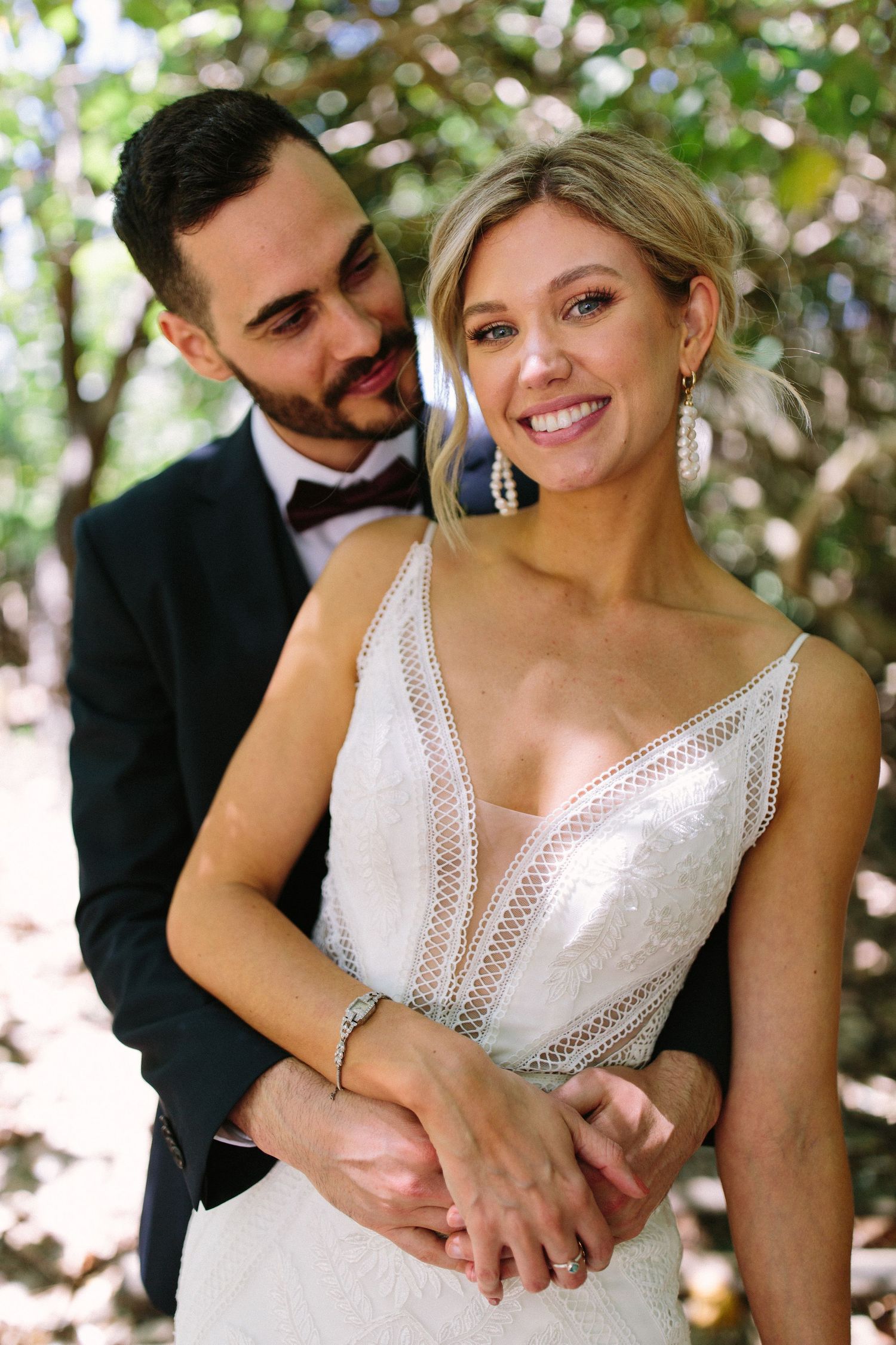 Romantic wedding couple moment captured in natural outdoor lighting under trees.
