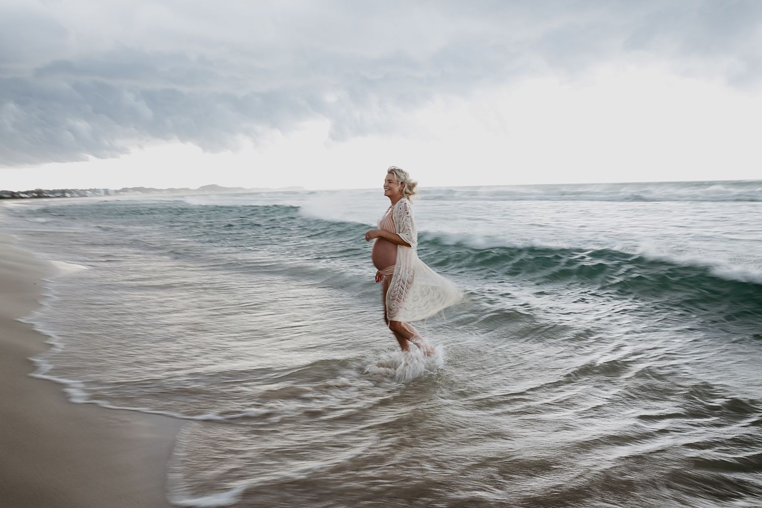 Person wading into gentle ocean waves on an overcast day.