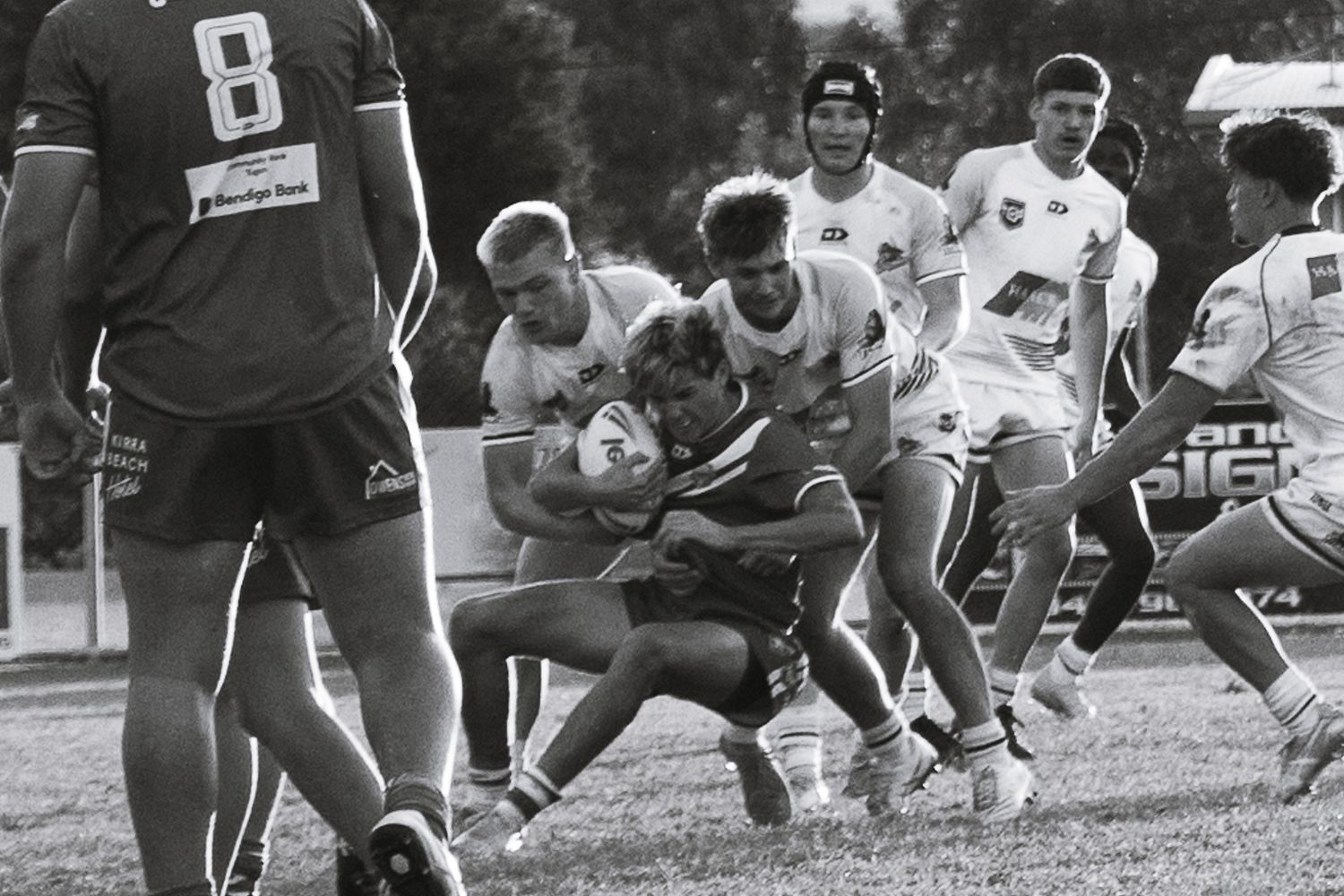 Black and white photo of a rugby match showing players engaged in a tackle during gameplay.