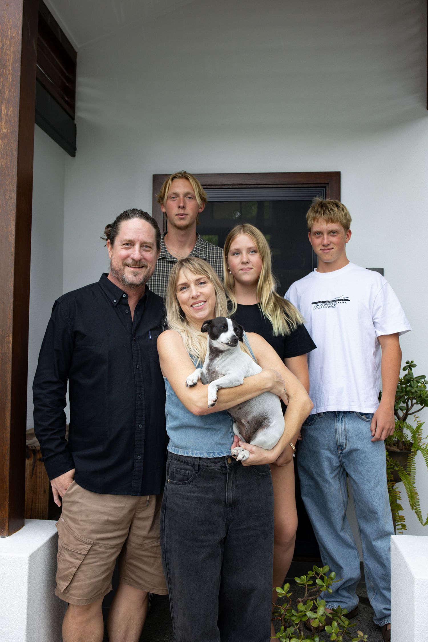 A group stands together on a porch while one person holds a small black and white dog.