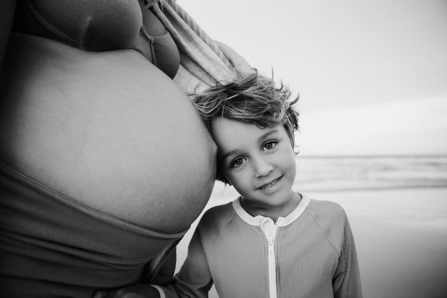 Black and white beach portrait with pregnant woman and child.