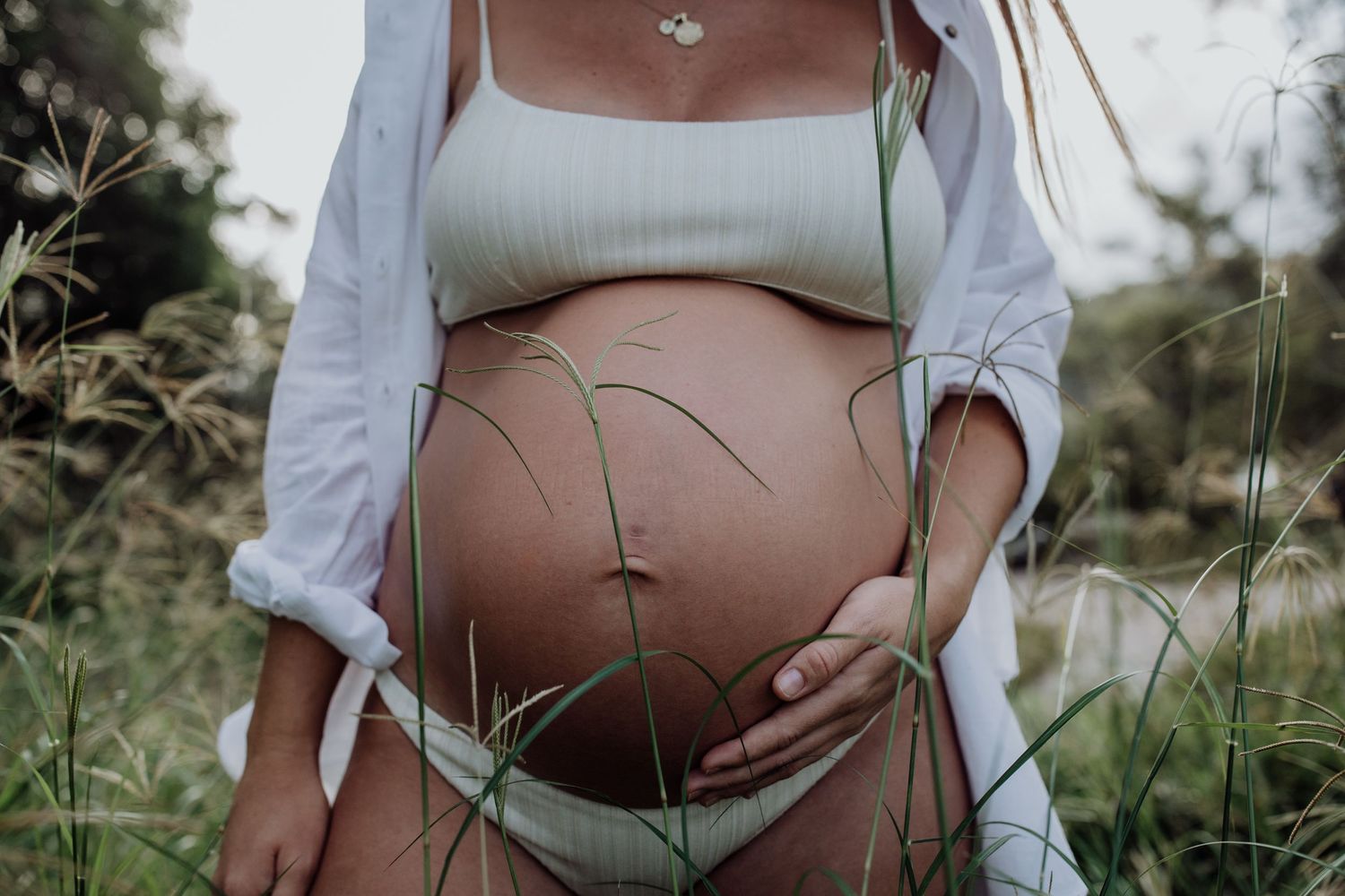Maternity photoshoot in natural setting showing pregnant belly among tall grass.