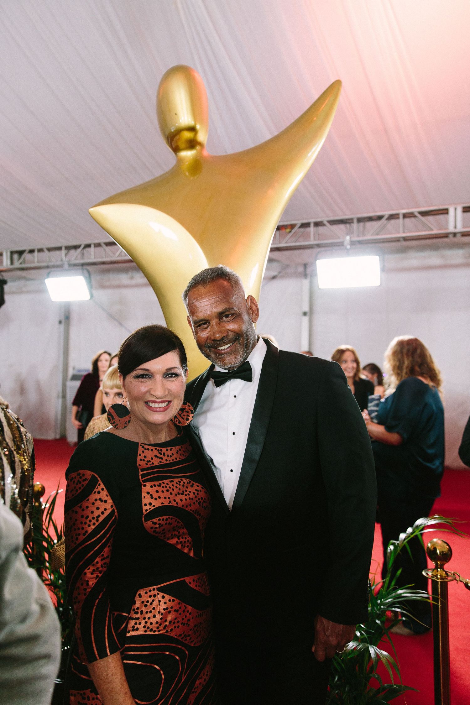 Attendees in formal wear posing beneath large golden star decorations at an awards ceremony.