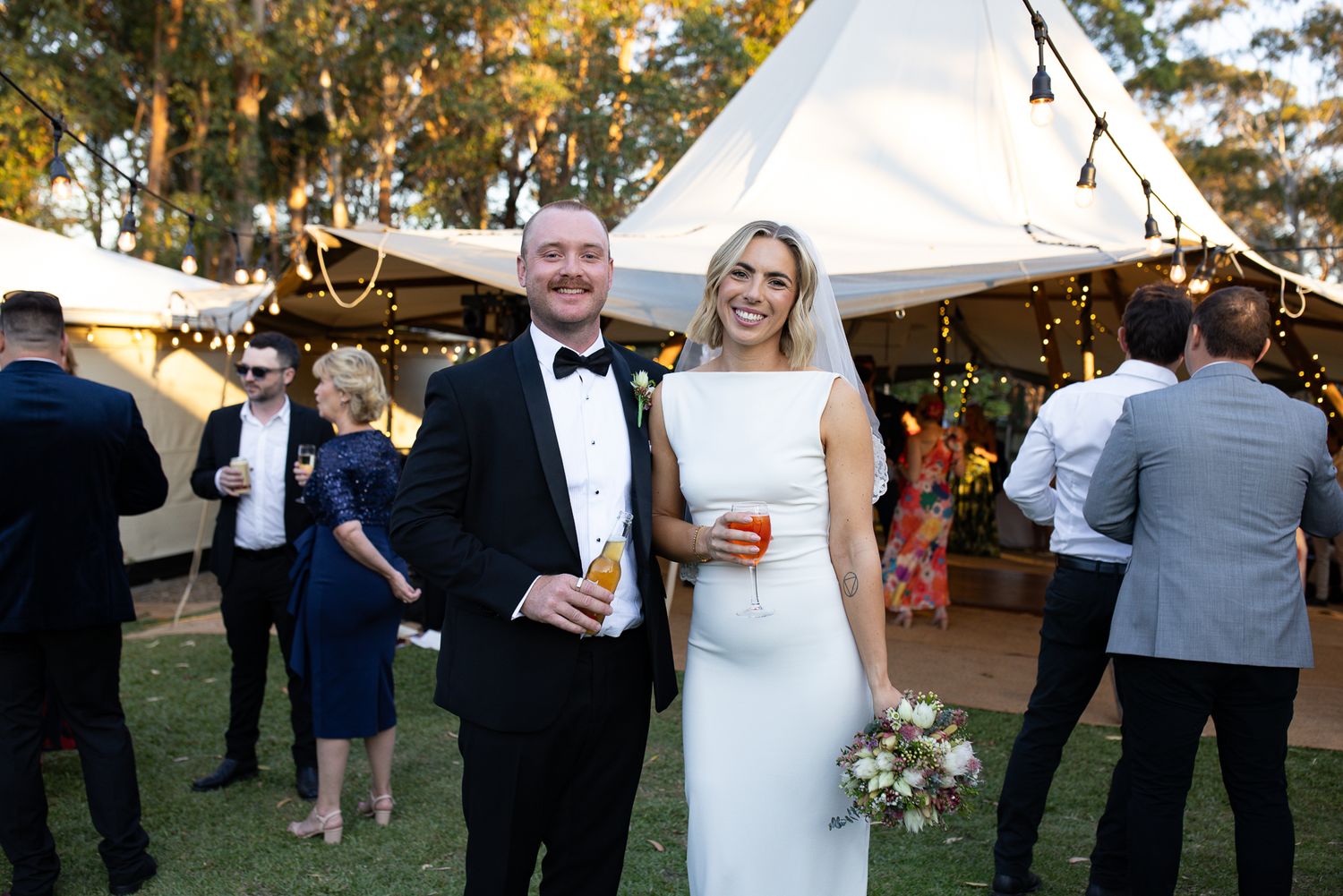 Outdoor wedding reception under white tent canopy with autumn trees in background.