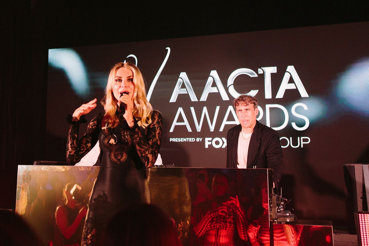 Performers on stage at an awards show with dramatic red lighting and AACTA branding visible.