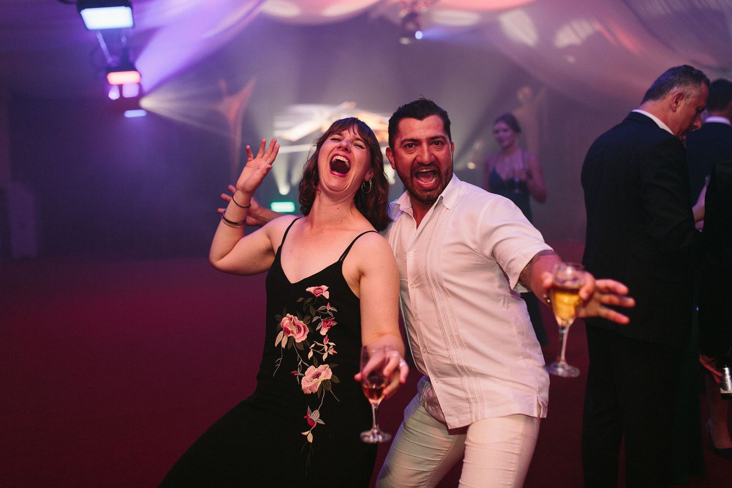 Guests dancing and celebrating at a dimly lit formal event with purple lighting.