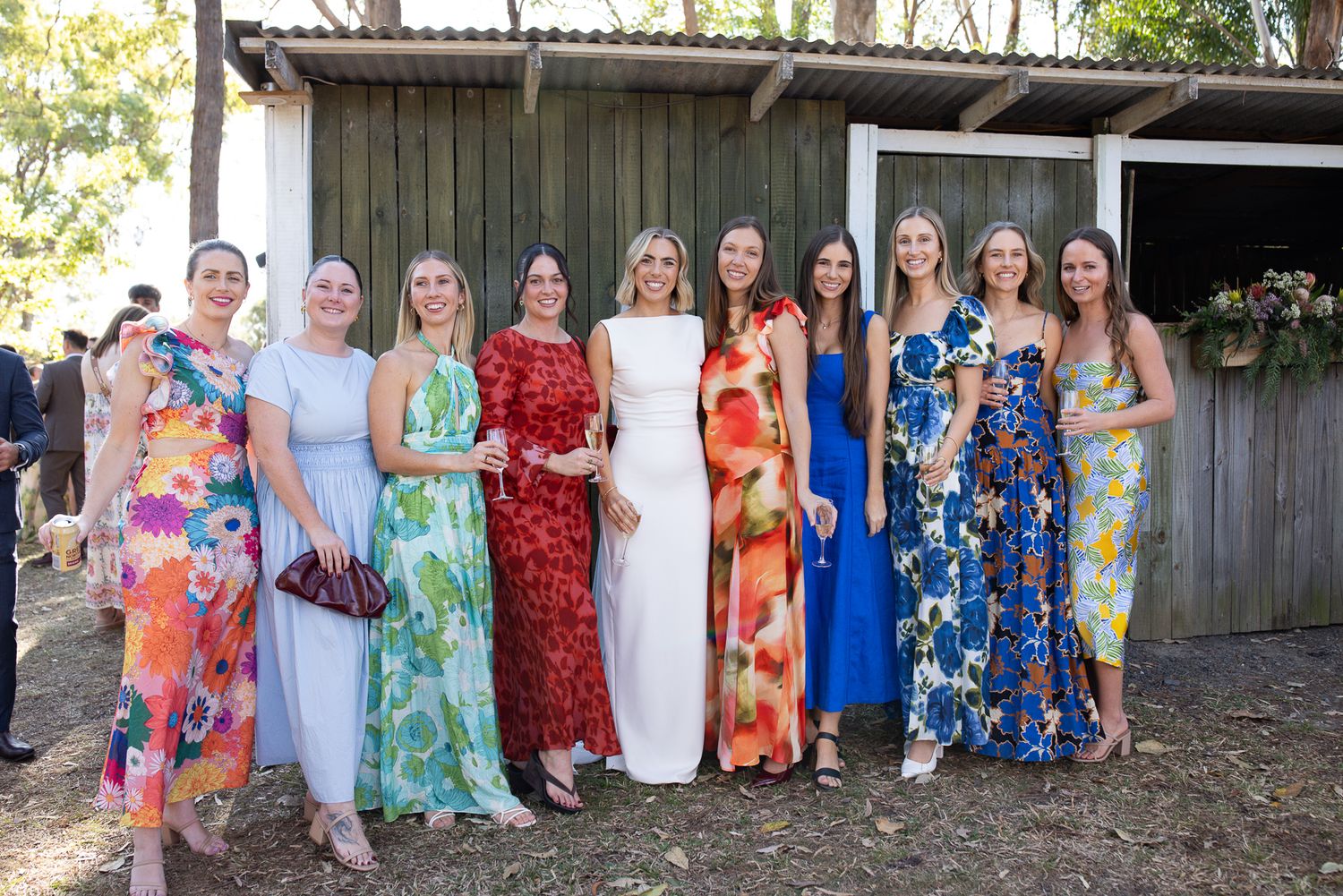 A group of women in colorful formal dresses pose together for a wedding party photo.