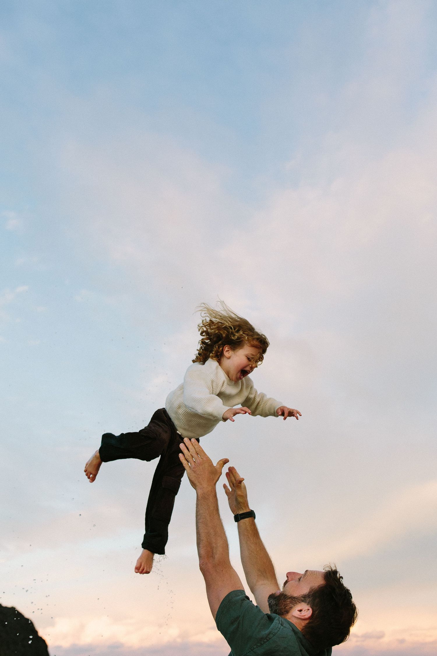 Parent lifting child playfully against sunset sky in joyful moment.