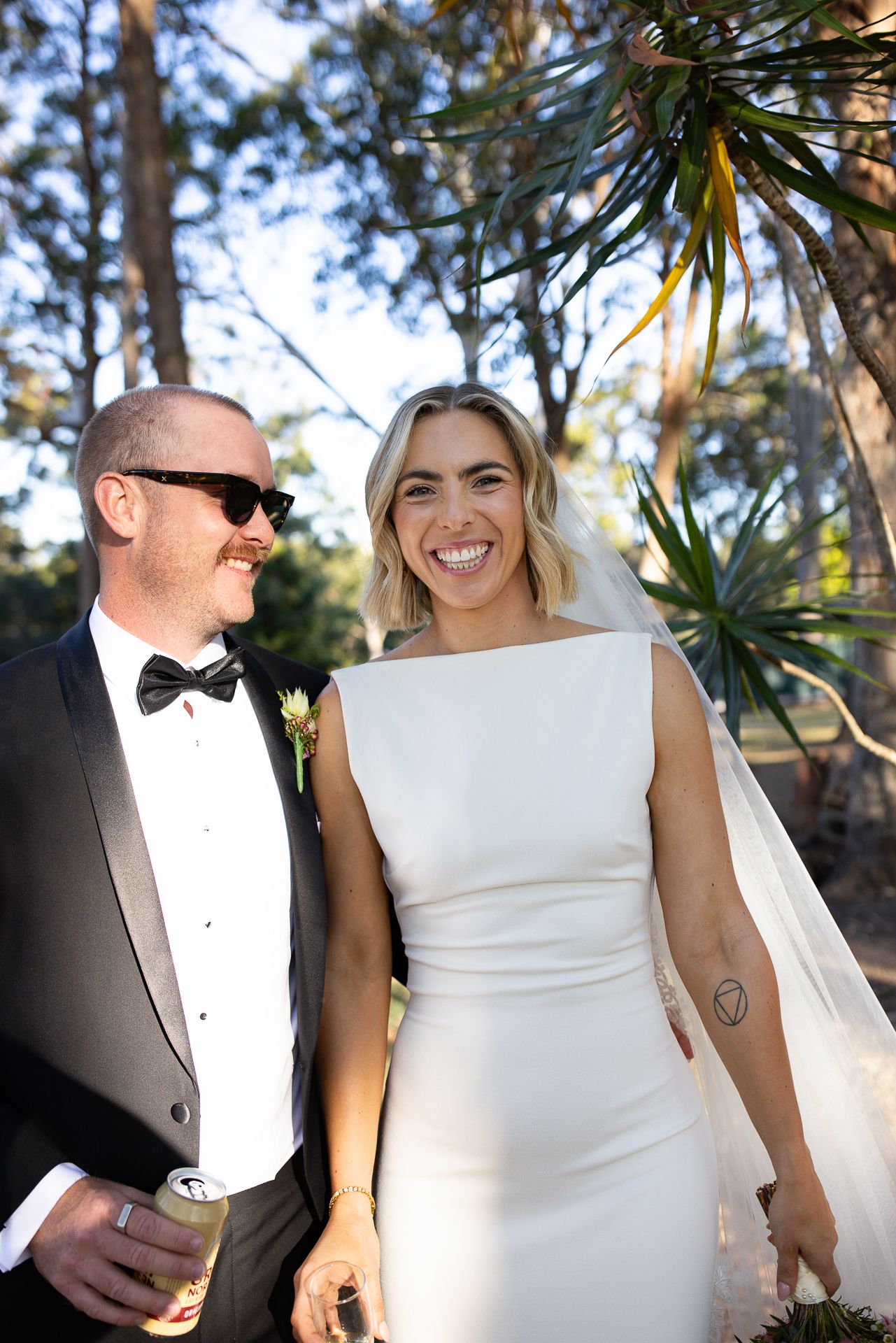 Elegant couple in formal wedding attire posing among tropical plants.