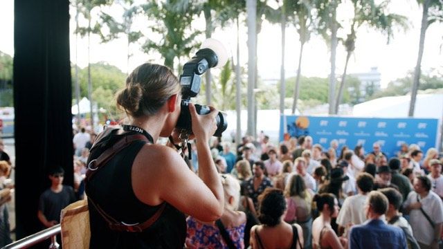 A large crowd gathered under palm trees at an outdoor event venue.