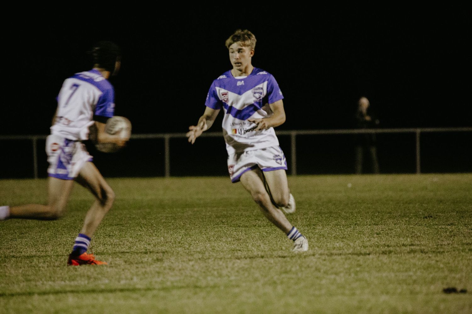 Rugby player in blue and white jersey running with the ball during a nighttime match.