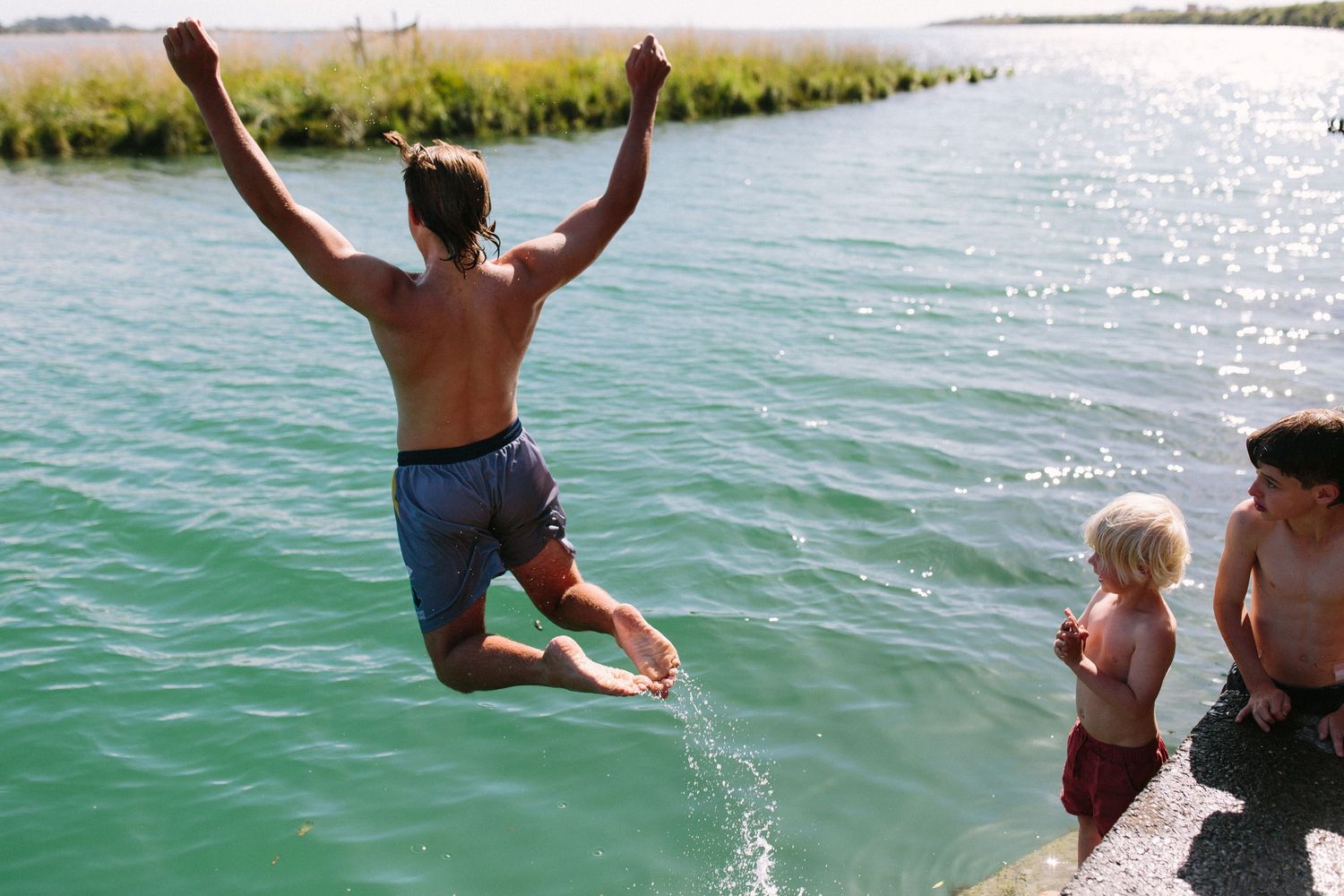 People jumping and diving into turquoise water on sunny summer day.