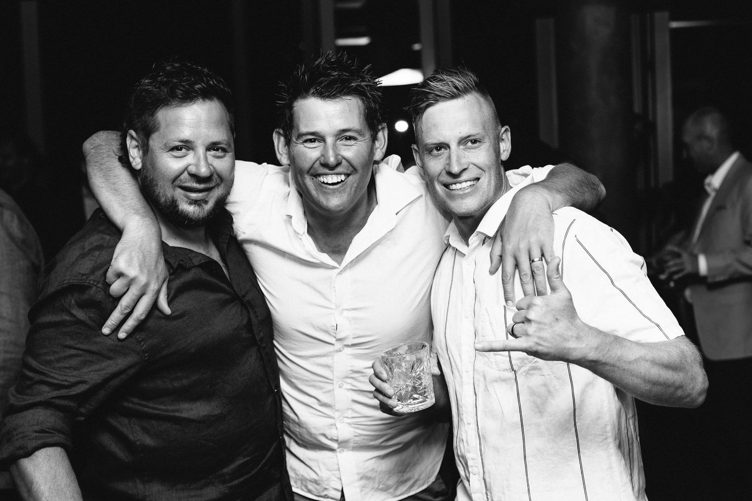 Three friends in formal attire share a candid black and white moment at a celebration.