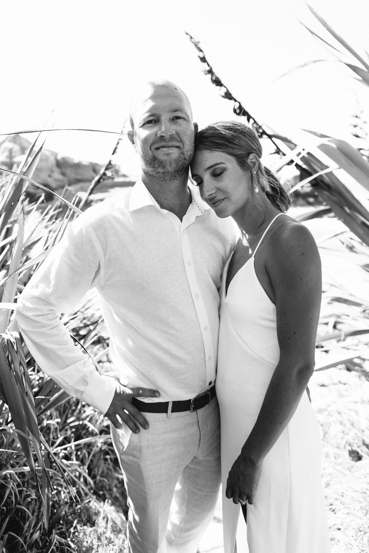 Black and white beach portraits of a couple in matching white outfits.