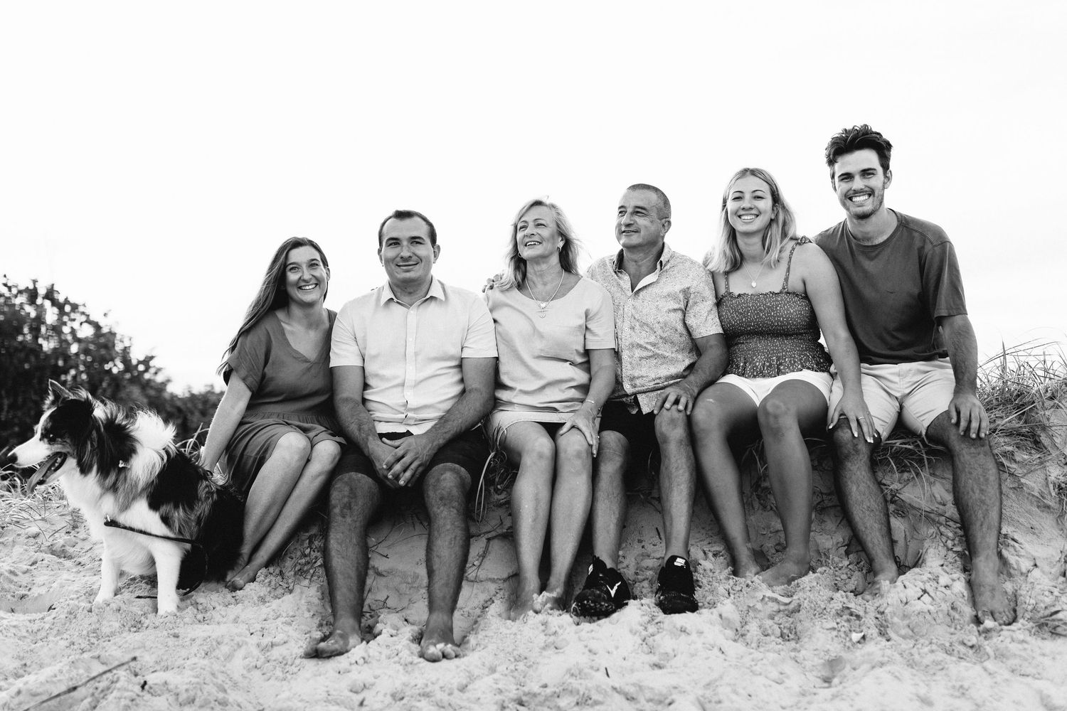 Black and white panoramic group photo of people sitting together on a beach or hillside.