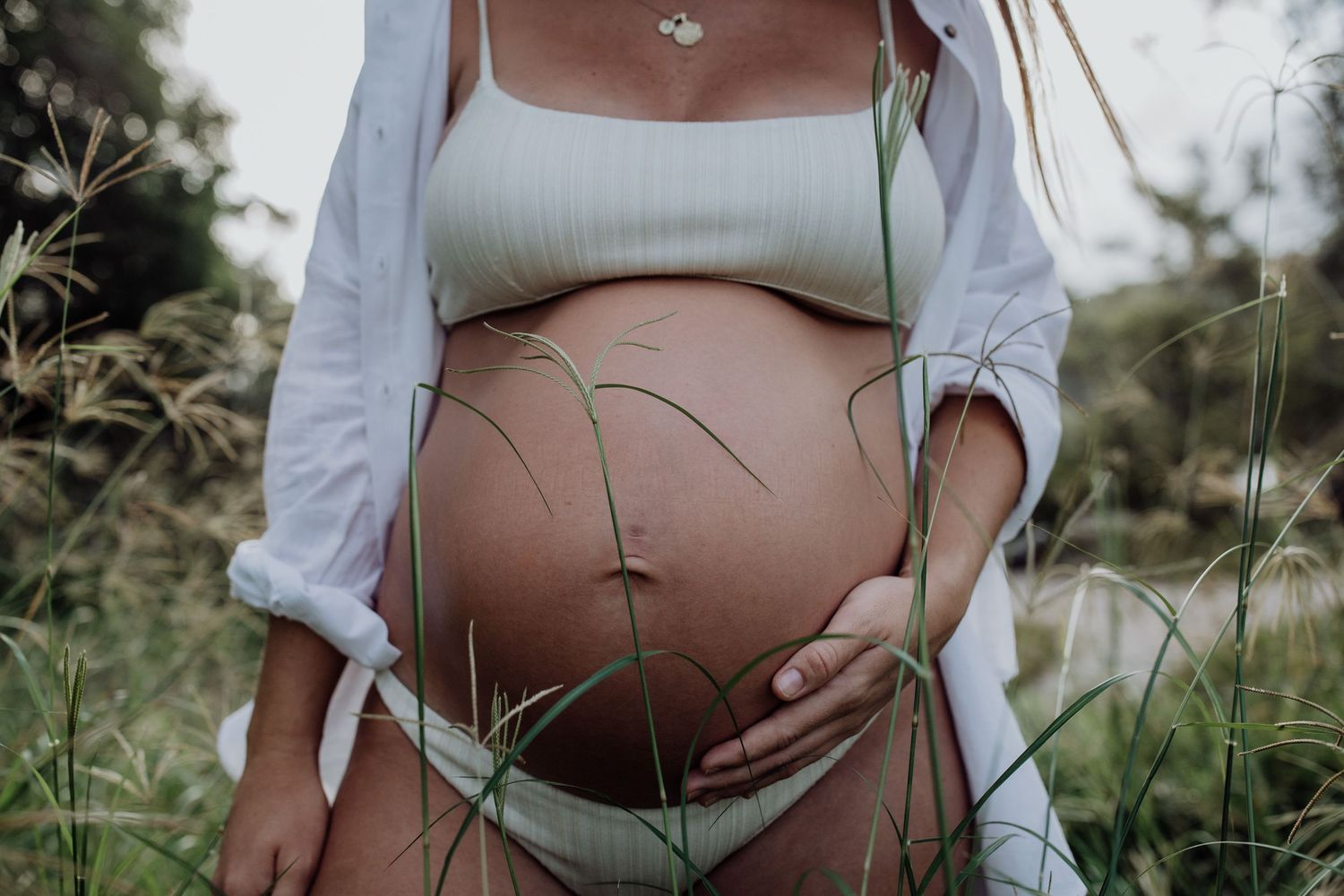 A series of artistic maternity photos showing a pregnant belly against tall grass and natural lighting.