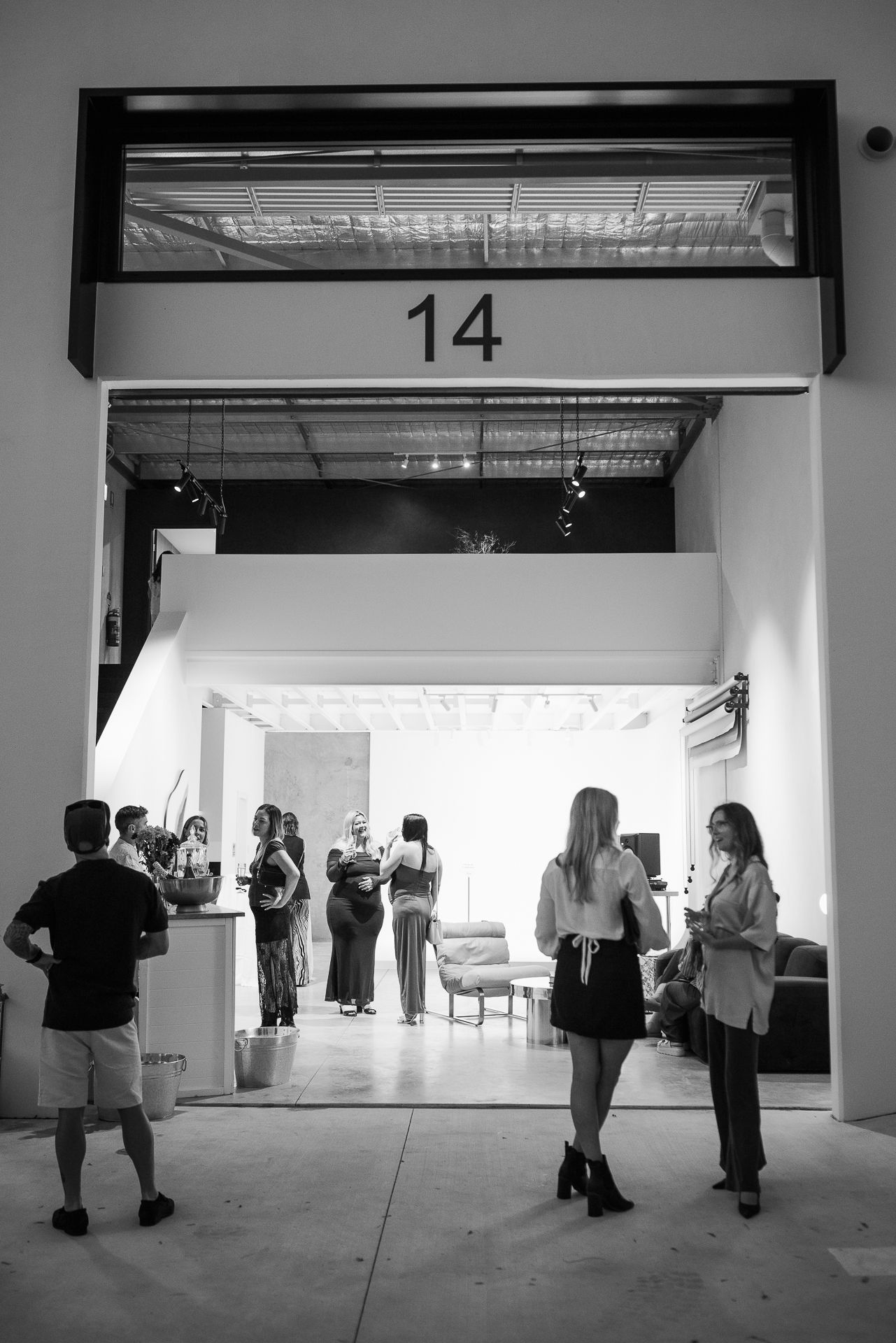 People gathering in a minimalist white gallery space with fluorescent lighting.