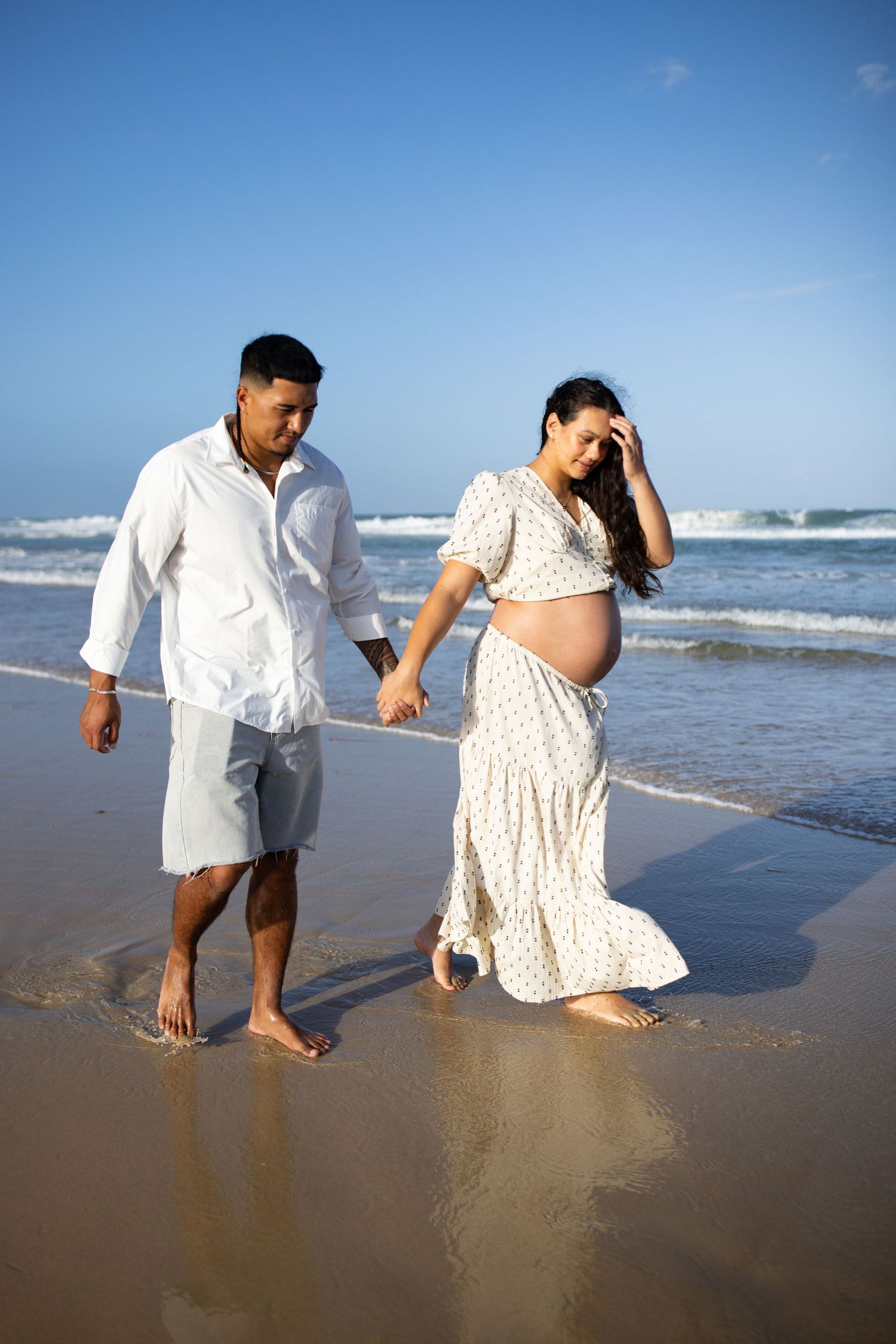 Couple walking together on a sandy beach, leaving footprints in the wet sand.