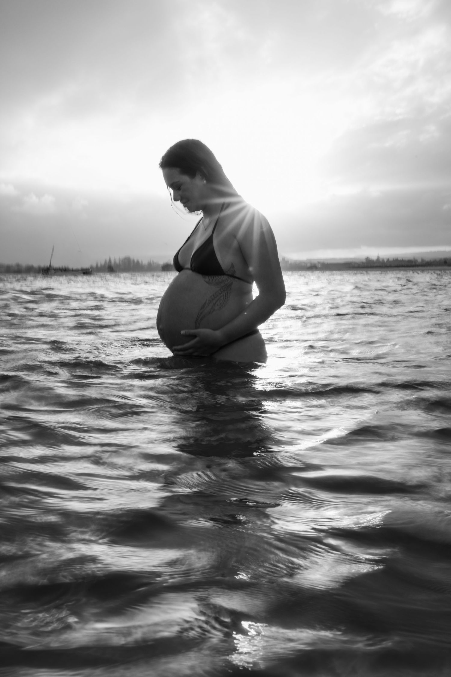 Black and white photos of a maternity session in ocean waves at sunset.