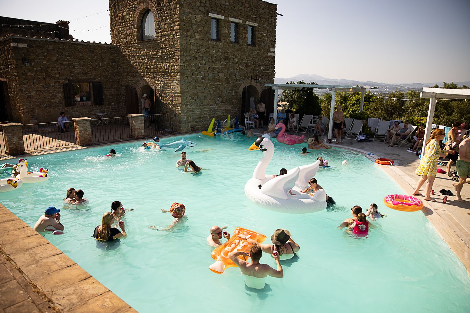 Panoramic view of people relaxing in a resort pool surrounded by stone buildings.