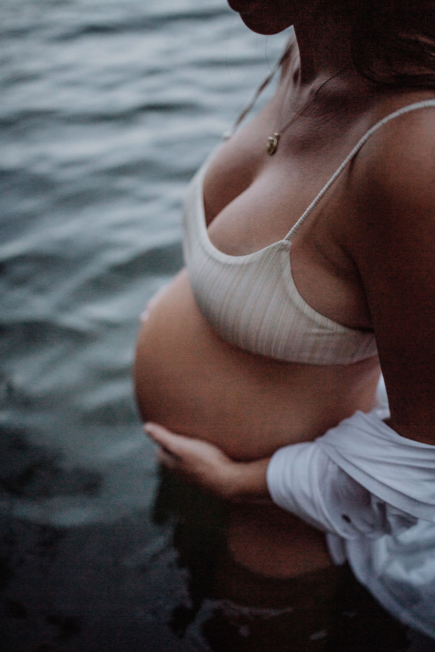 Artistic close-up shots of a pregnant belly silhouetted against water.