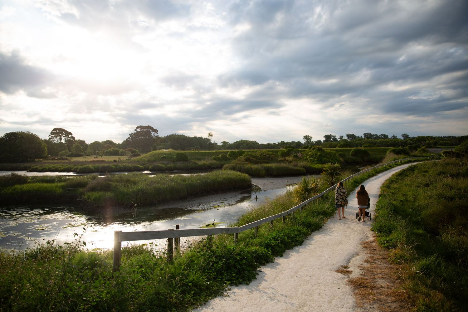 Scenic coastal path winding along marshland under dramatic cloudy sky.