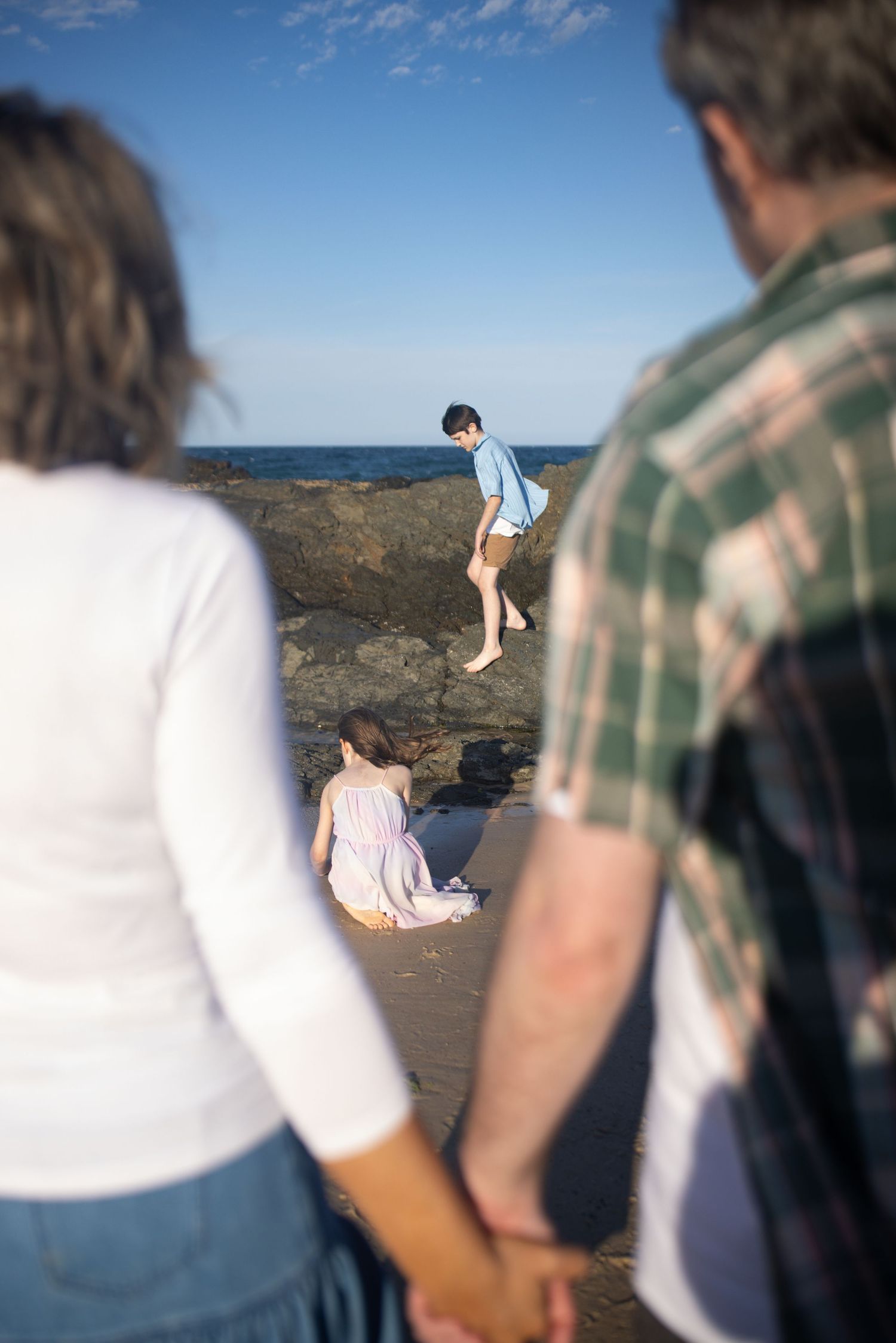 People watching someone balance on coastal rocks at the beach.