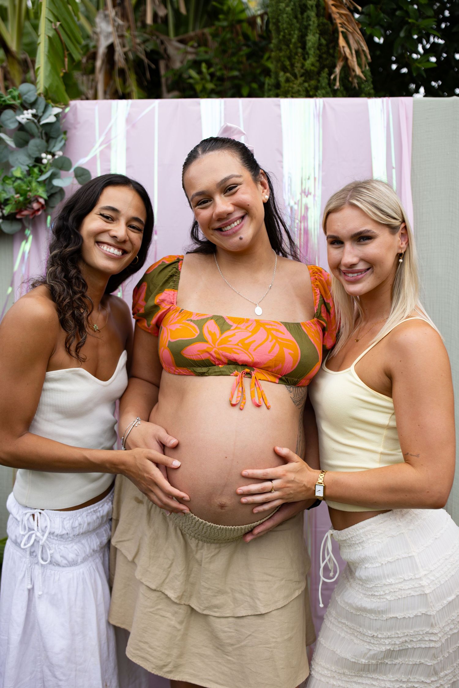 Friends gather around expectant mother with painted butterfly design on baby bump.