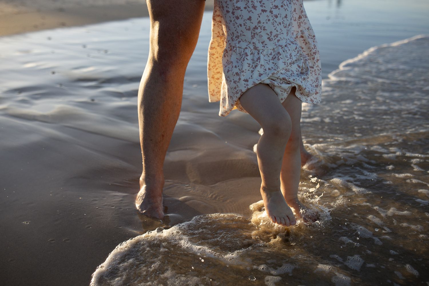 Bare feet walking along a sandy beach at sunset with waves gently rolling in.