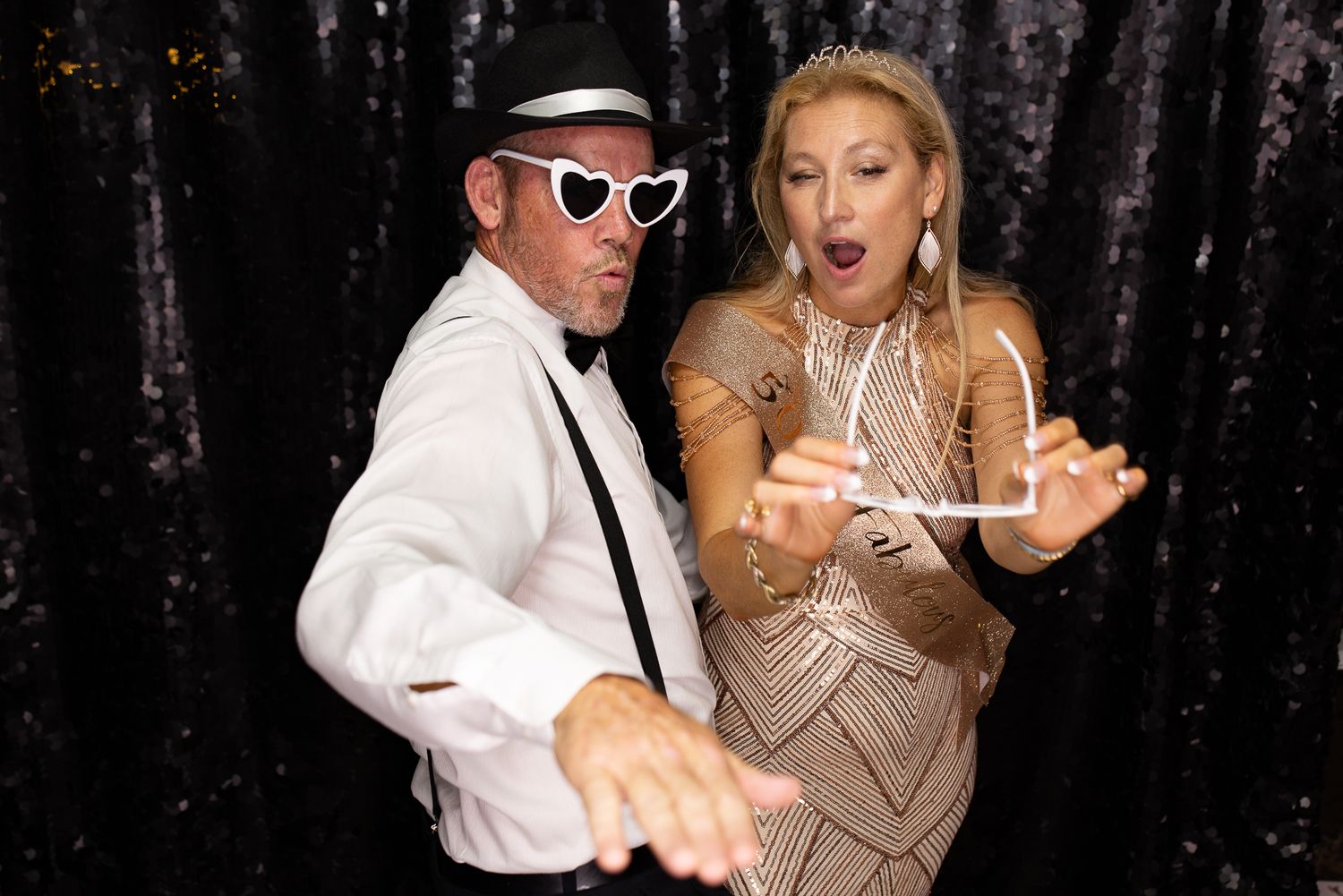 A couple dancing and having fun at a party with a sparkly backdrop.