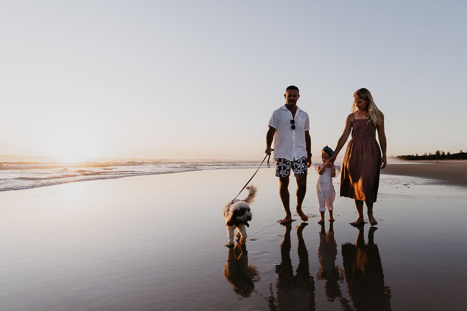Silhouetted family walking along reflective beach at sunset.